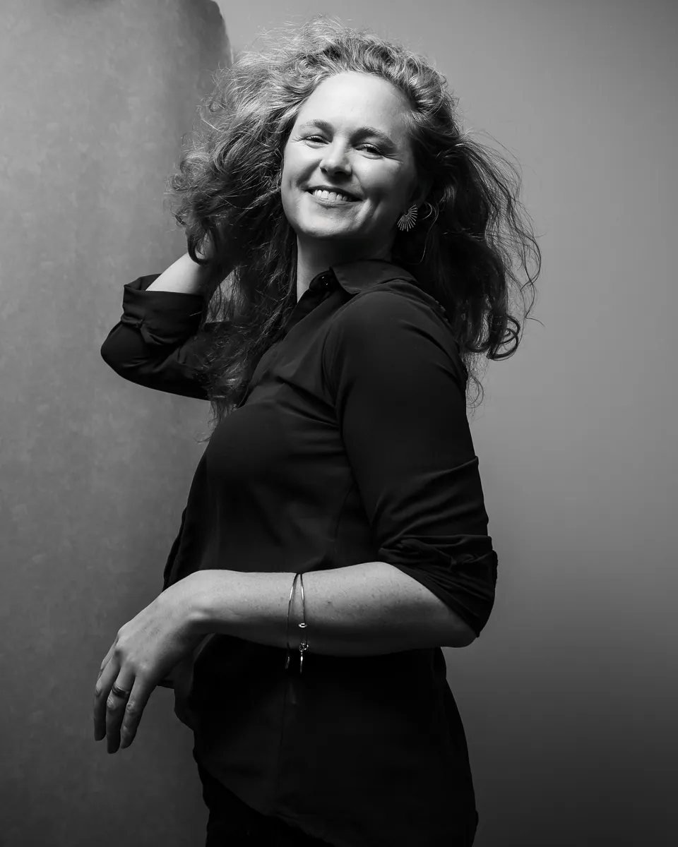 Frau mit fliegenden Locken dreht sich lachend vor dem Studiohintergrund