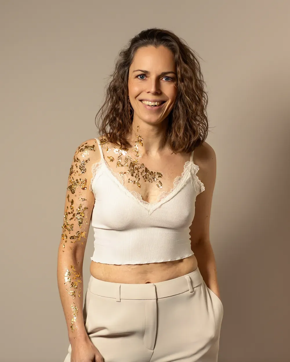 Juliane Klüß lacht in die Kamera, ihre Narben an Arm und Brust sind mit Blattgold belegt