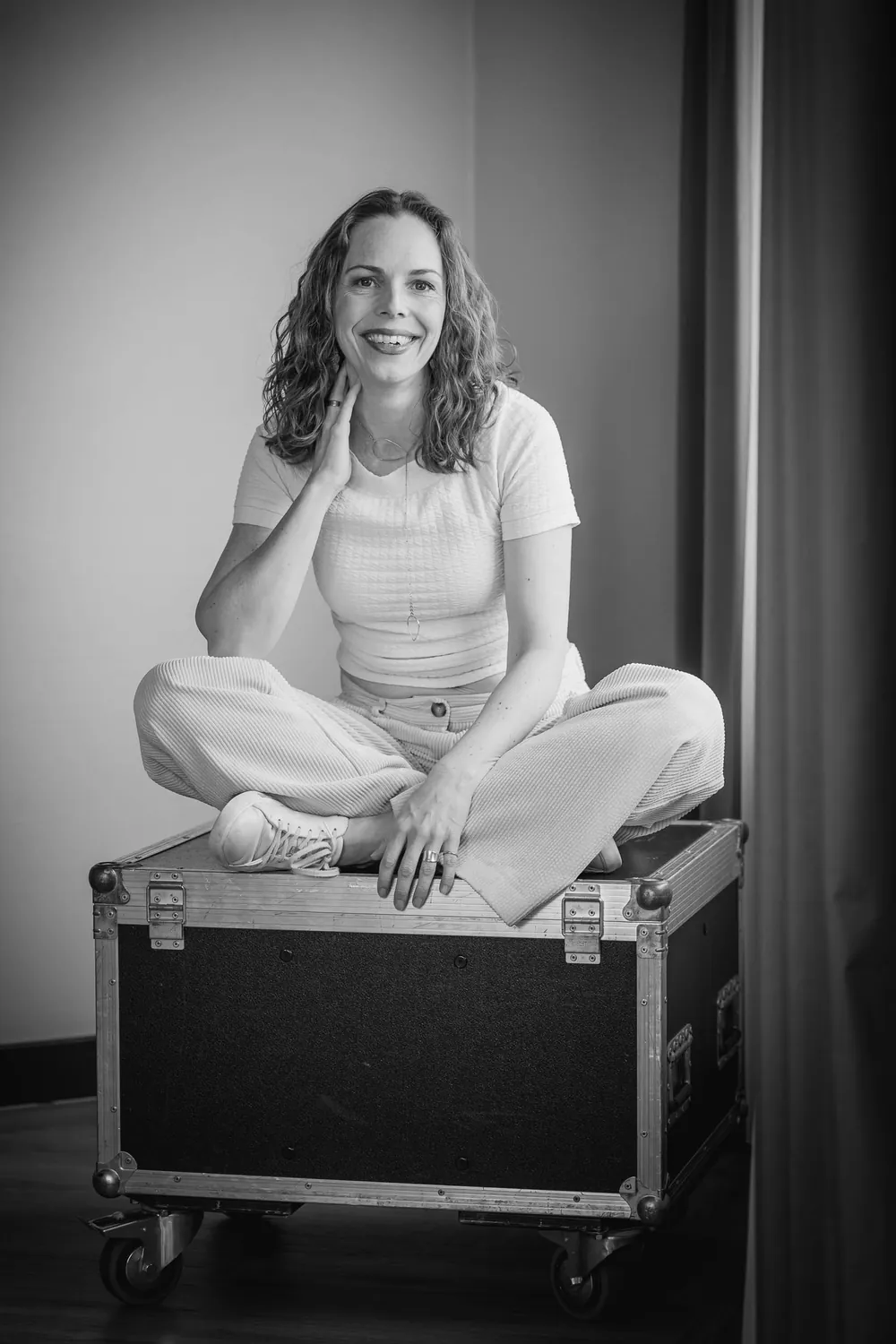 Juliane Klüß sitzt lachend im Schneidersitz auf einem Flightcase, Schwarz-Weiß-Porträt